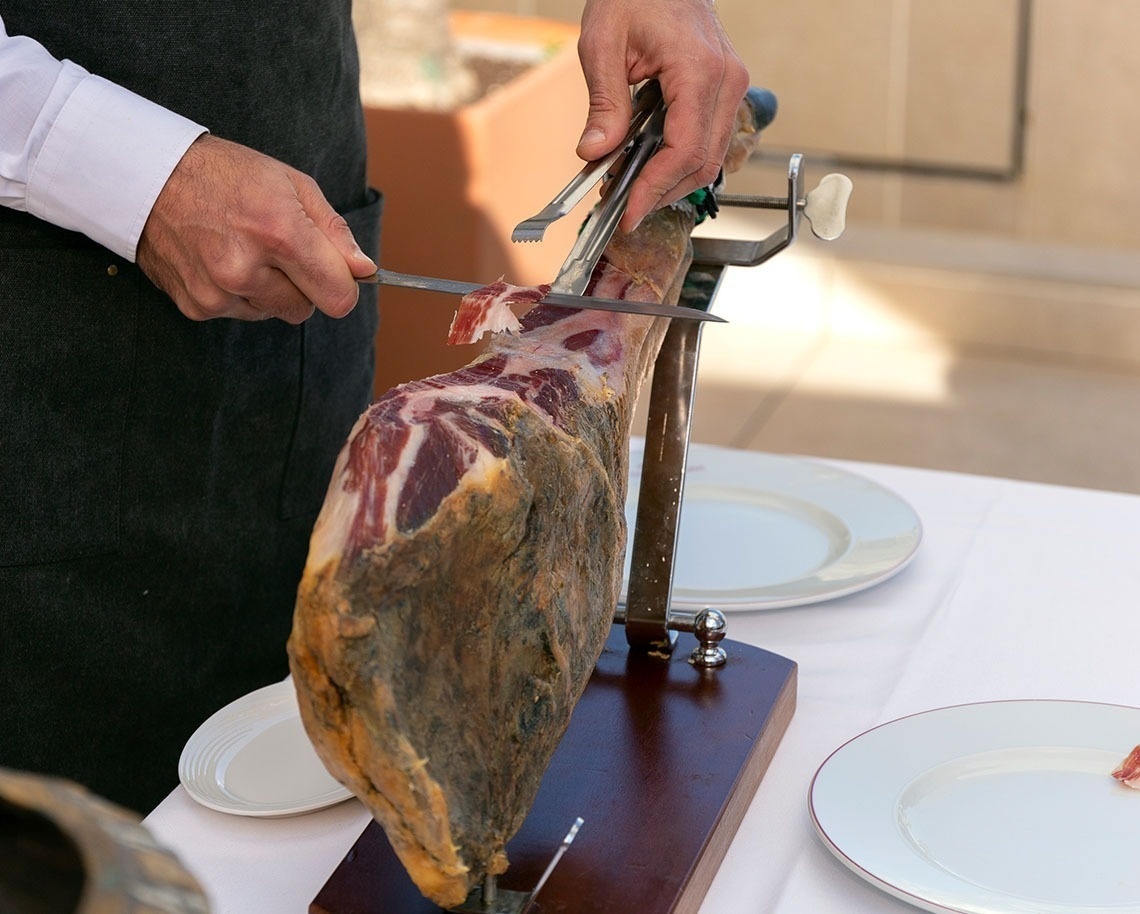 un hombre corta un trozo de jamón con un cuchillo