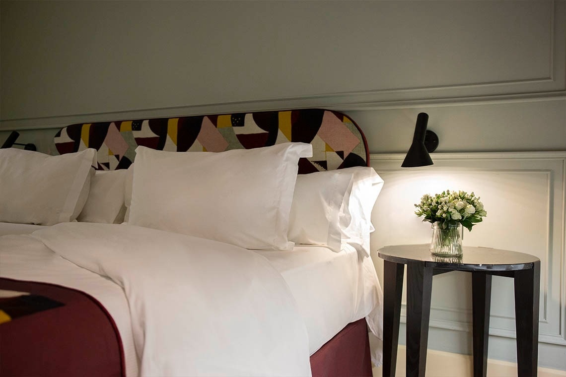 una cama con sábanas blancas y una mesa con un jarrón de flores