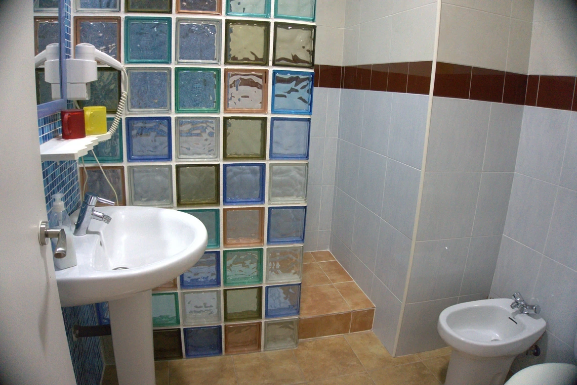Baño moderno con lavabo, bidet, paredes de azulejos y ventana de bloques de vidrio para el Casual Alquimia Cádiz.