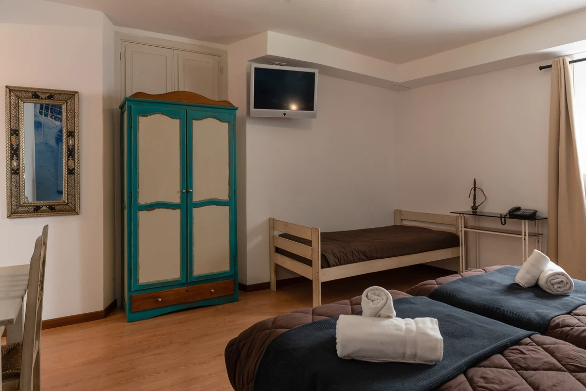 Habitación de hotel con Casual Alquimia Cádiz, armario azul, espejo y dos camas individuales.
