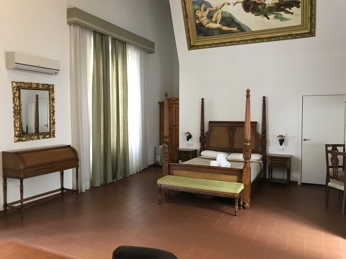 Elegante habitación de hotel con cama con dosel,Casual Alquimia Cádiz escritorio antiguo y cuadro de Miguel Ángel.