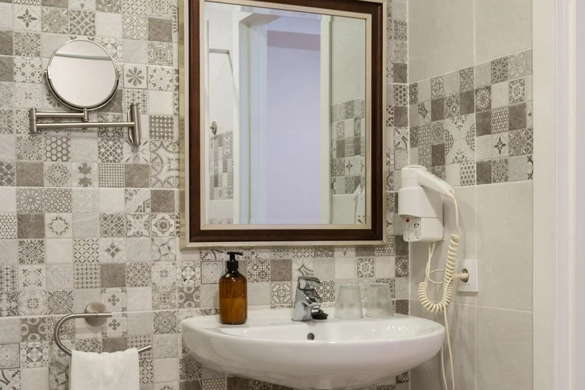 Lavabo moderno con espejo y secador de pelo en un baño con azulejos decorativos. Casual Alquimia Cádiz