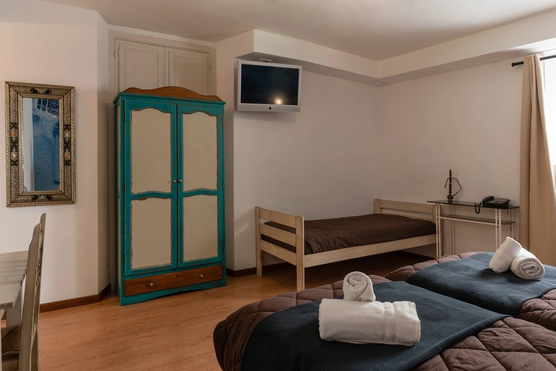 Habitación de hotel con cama, armario azul, TV y espejo. Casual Alquimia Cádiz