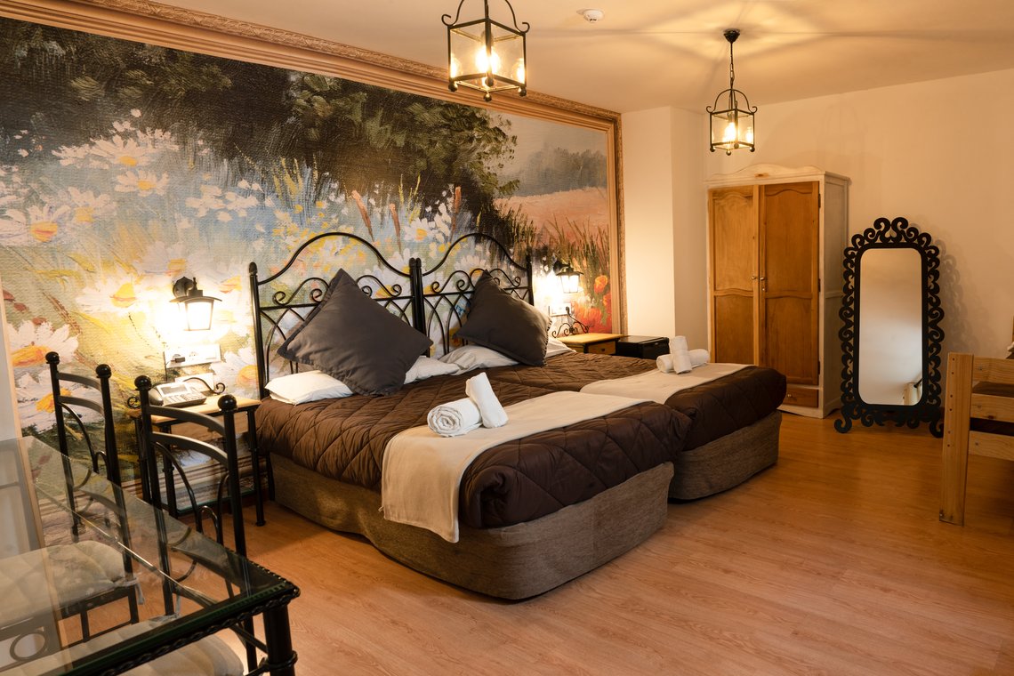 Habitación acogedora con mural de flores, dos camas y armario de madera. Casual Alquimia Cádiz