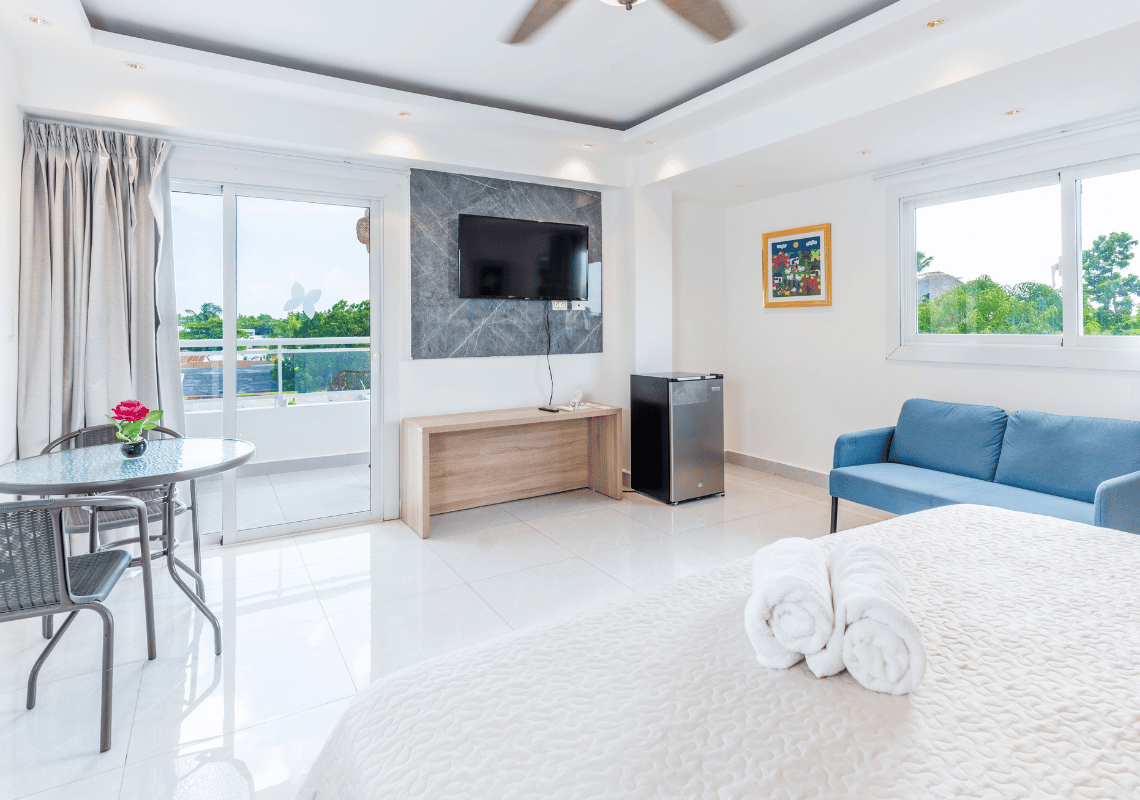Habitación con balcón, sofá azul y TV, ideal para tu Casual: On The Beach Bayahibe.