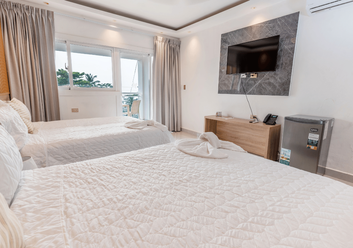 Cama con toallas en forma de cisne en hotel Casual: On The Beach Bayahibe, vista al balcón y TV.