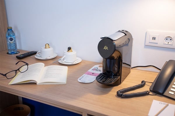 een koffiezetapparaat staat op een houten tafel naast een boek en een telefoon