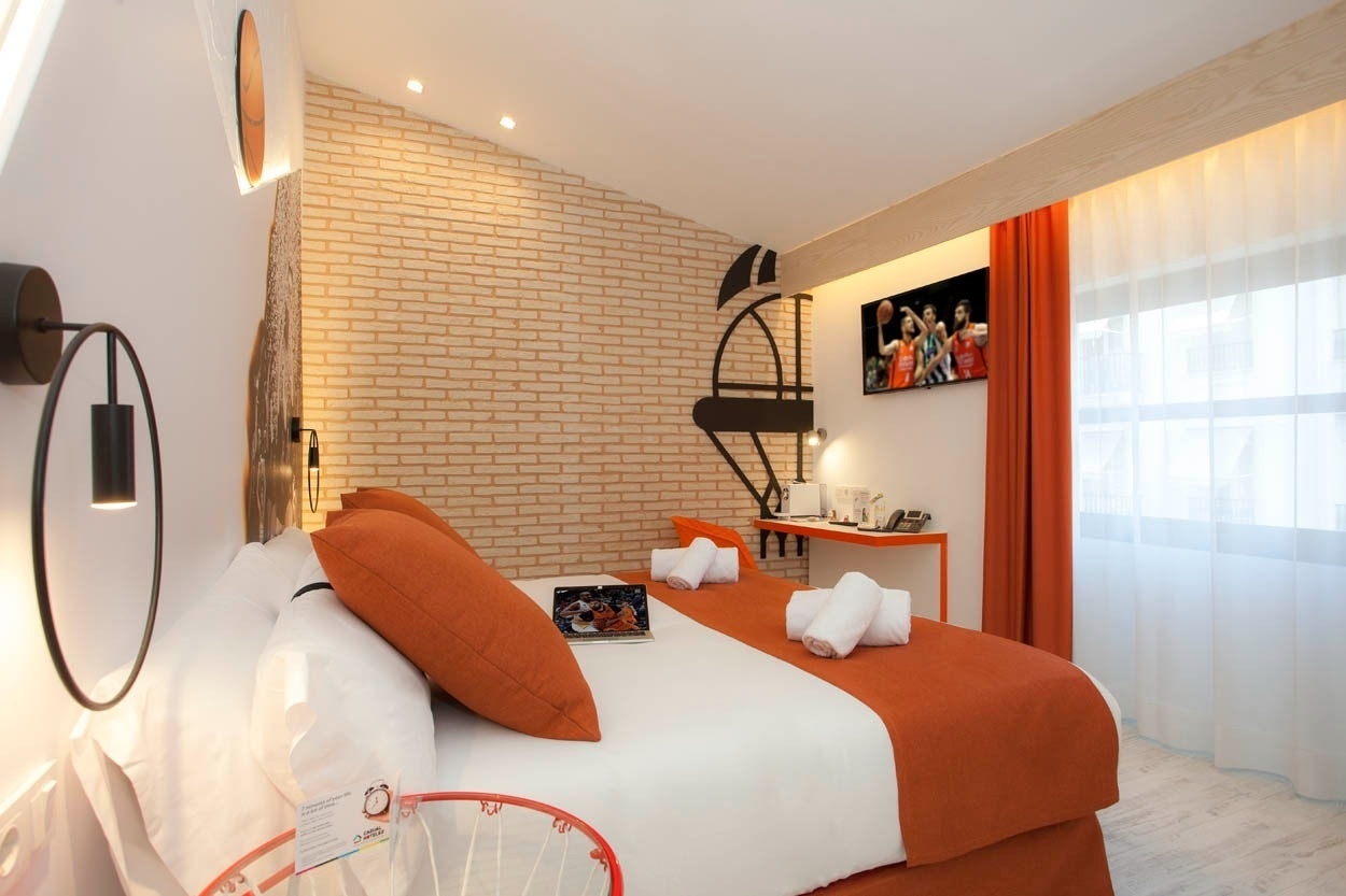Habitación moderna en Casual Socarrat Valencia: cama con mantas naranjas, TV y escritorio.