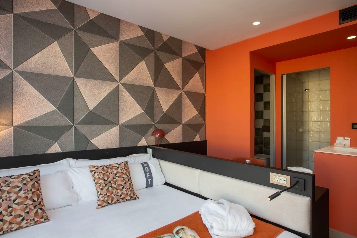Modernes Hotelzimmer mit geometrischer Wandgestaltung, orangefarbenen Akzenten und einer Dusche. Ideal für Ihren Aufenthalt im Casual Kubic Athens - Smart Hotel im Zentrum von Athen.
