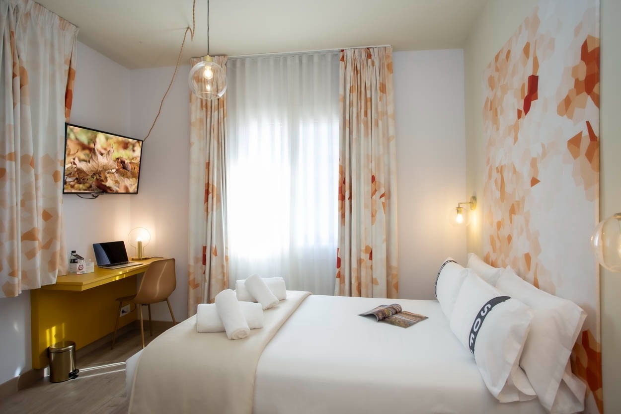 Comfortabele hotelkamer Casual Colours Barcelona met bureau, tv en bed met witte lakens.