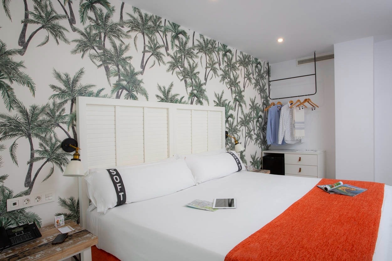 Tropisches Zimmer im Casual del Mar Málaga mit Palmen-Tapete und orangefarbener Tagesdecke. Zentral gelegen.