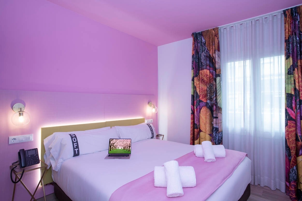 Een stijlvolle hotelkamer met paarse muren, een comfortabel bed met zachte dekens en een laptop, gelegen in Casual Colours Barcelona.
