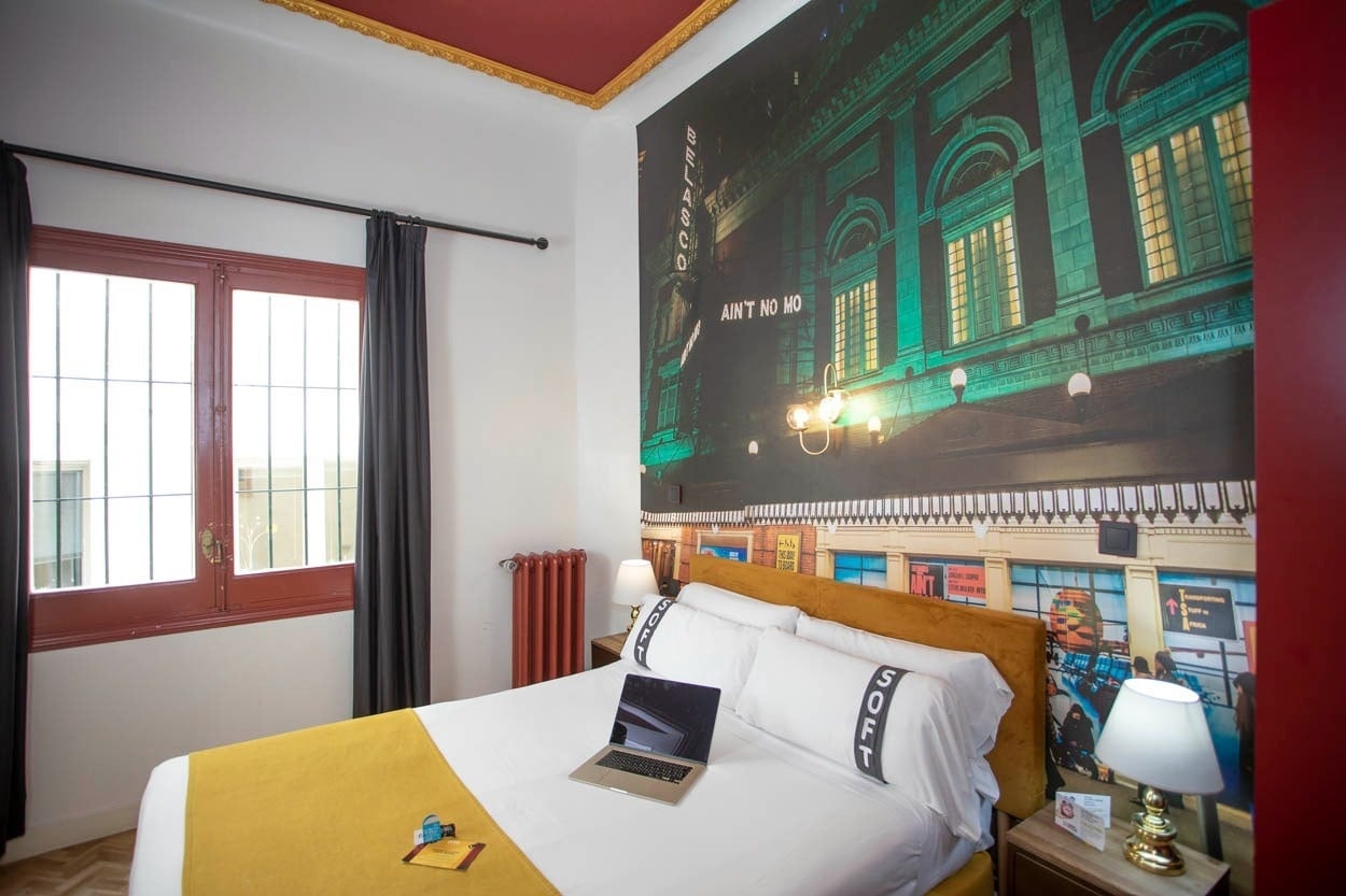 Gemütliches Schlafzimmer im Casual del Teatro Madrid mit Wandbild, Doppelbett und Laptop.