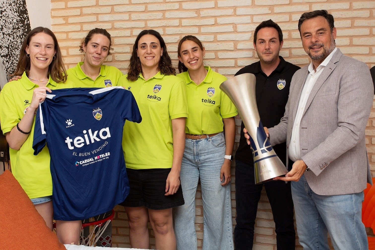 un hombre sostiene un trofeo junto a un grupo de personas con camisetas de teika