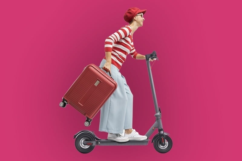 a woman is riding a scooter with a suitcase on the back