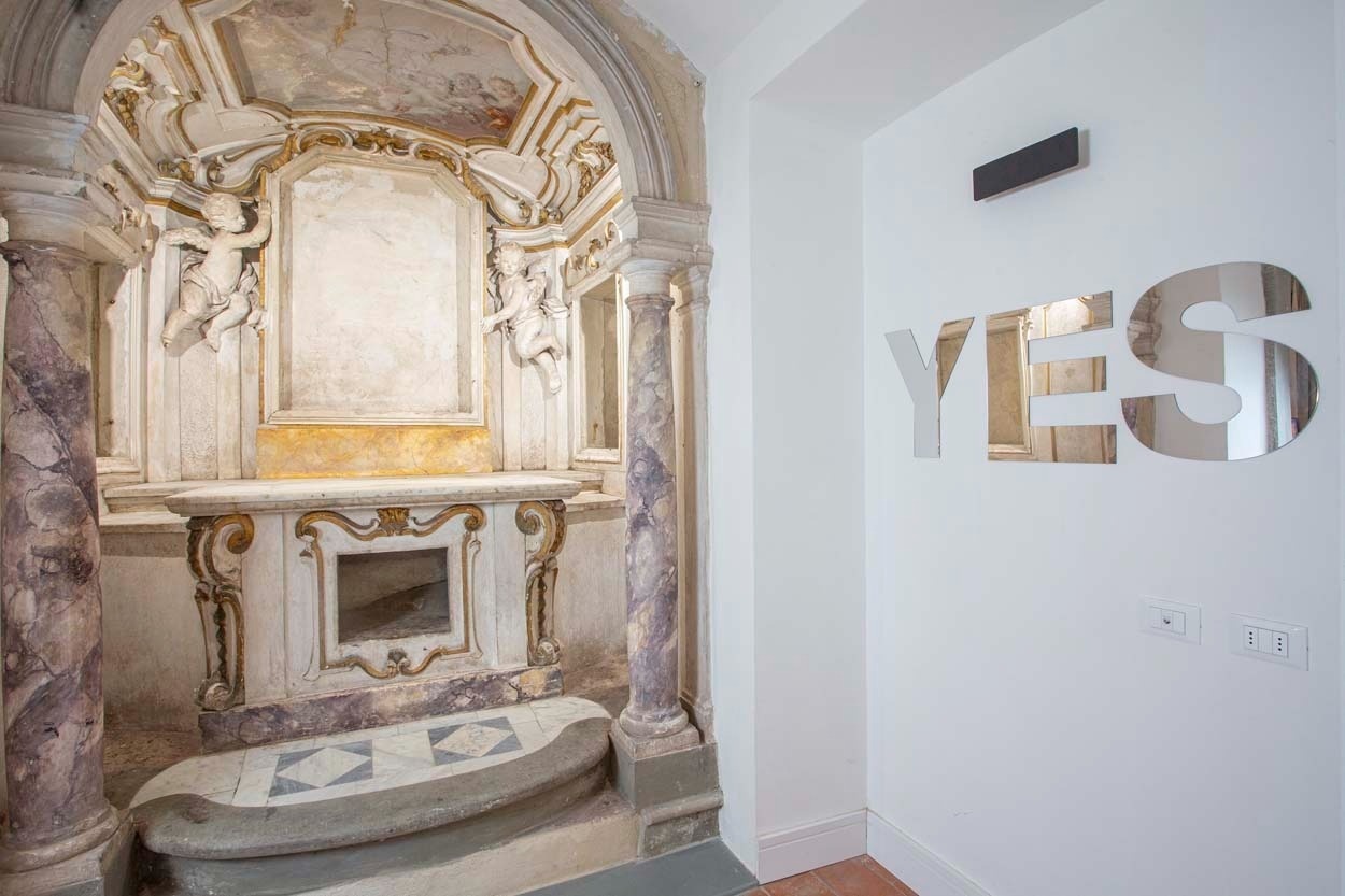 Dekorative Engel über einem barocken Altar; moderne 'YES'-Schriftzüge an der Wand über Steckdosen. Casual Rinascimento Firenze - Zentrales Hotel mit Pool in Florenz.