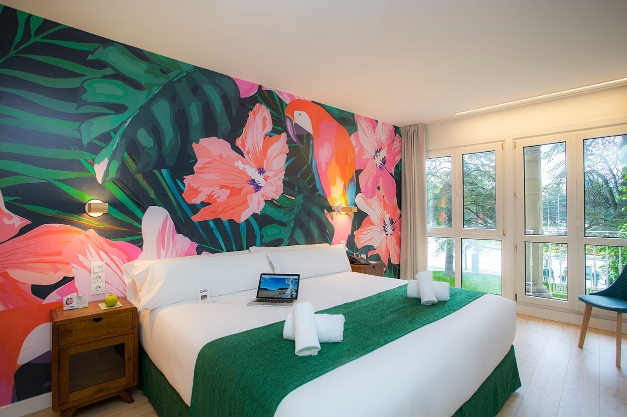 Tropisches Schlafzimmer im Casual de las Olas San Sebastián - Themenhotel. Dschungelmotiv an der Wand, Doppelbett, Laptop, Handtücher.