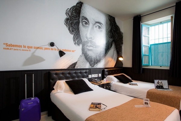 a room with two beds and a painting of hamlet on the wall