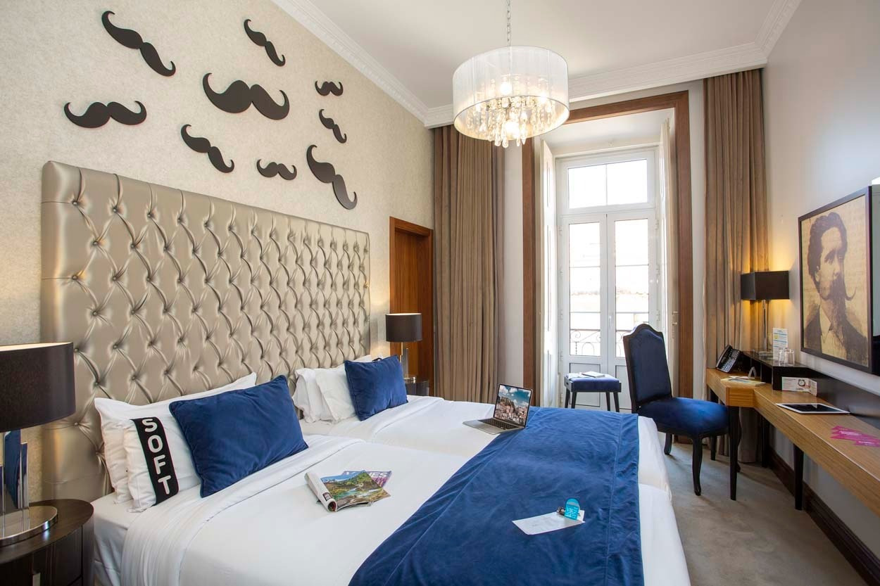 Gemütliches Schlafzimmer mit zwei Betten, blauem Akzent und Moustache-Wanddeko. Casual Belle Époque - Boutique-Hotel im Zentrum von Lissabon | Casual Hoteles