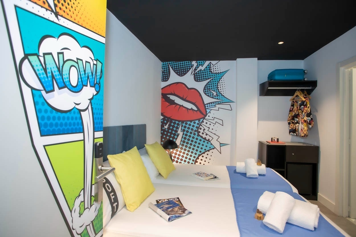Casual Pop Art Benidorm: Hotel im Comic-Stil mit Doppelbett, gelben Kissen und Comic-Wandmalerei.