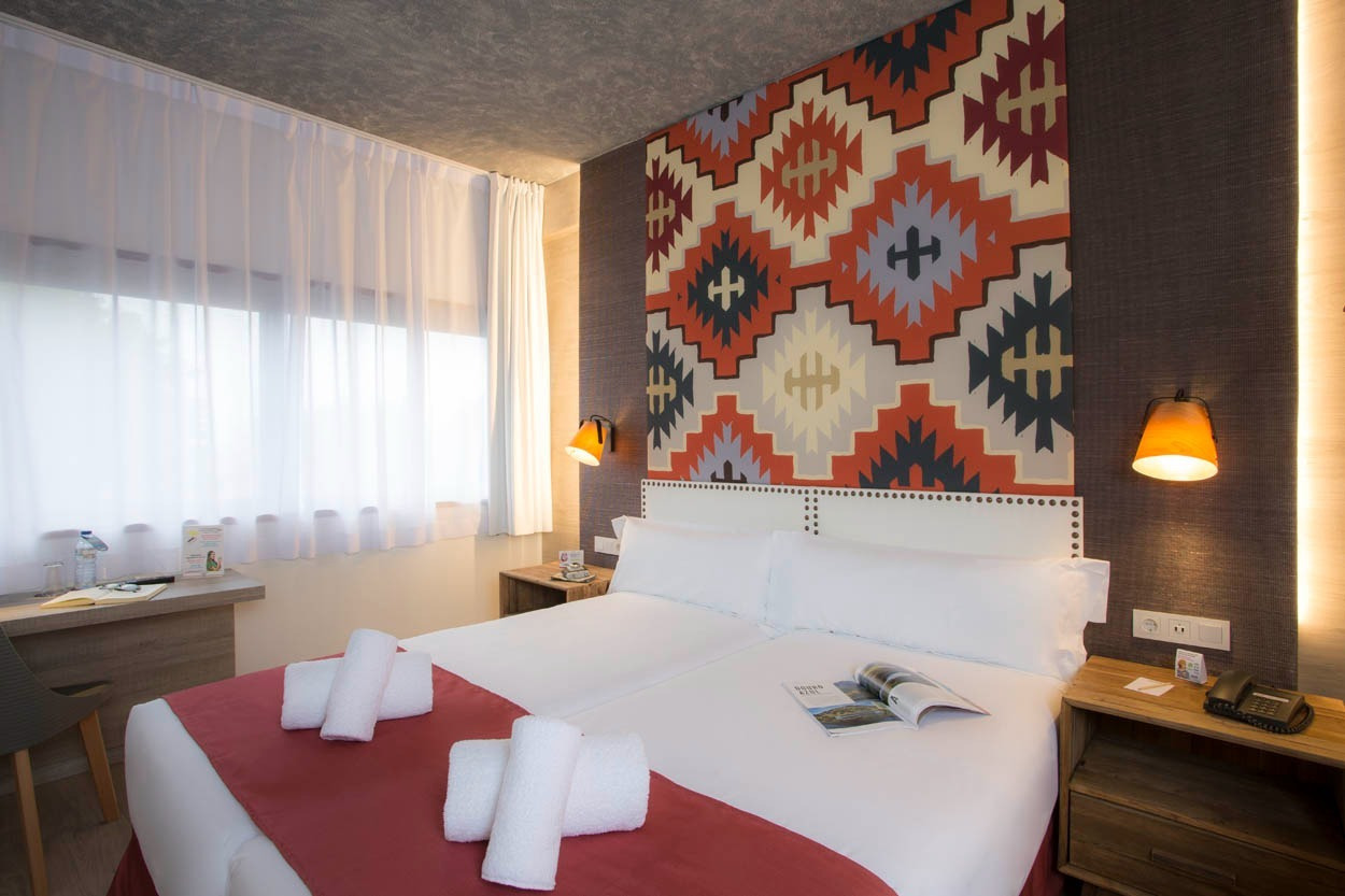 Doppelzimmer im Casual Inca Porto mit Musterwand und orangefarbenen Lampen.