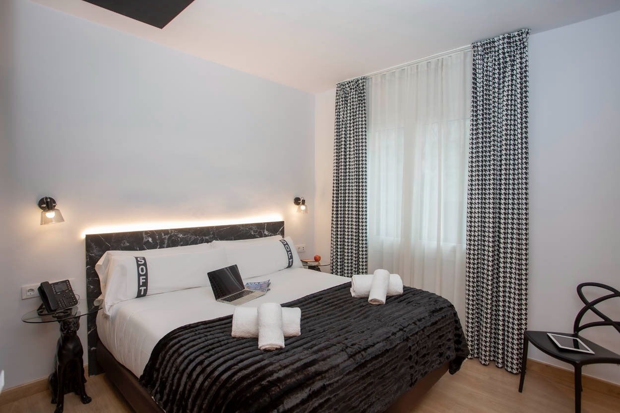 Moderne slaapkamer in Casual Colours Barcelona - Hotel nabij Sants, met zwart-wit hondenbotprint gordijnen en luxe beddengoed.