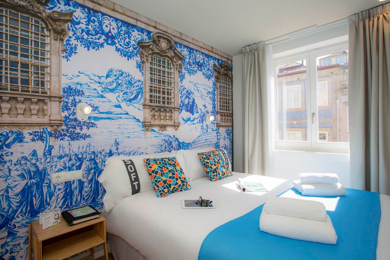 Camera accogliente con letto matrimoniale, cuscini colorati e murale ispirato a Porto presso Casual Raízes Porto - Boutique hotel vicino a Santa Catarina.