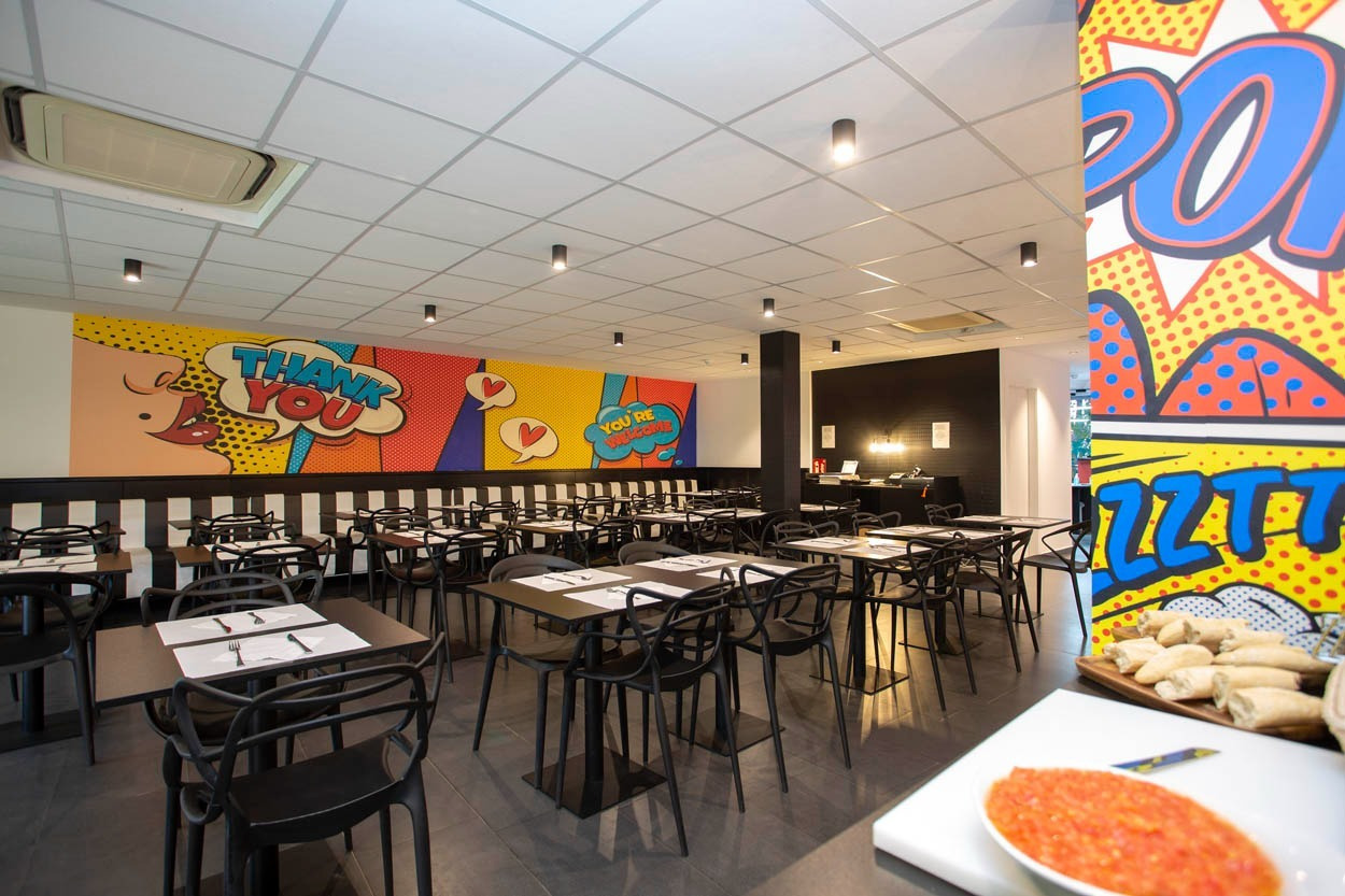 Blick in das Restaurant des Casual Pop Art Benidorm Hotels mit Comic-Wandmalereien und modernen Tischen.