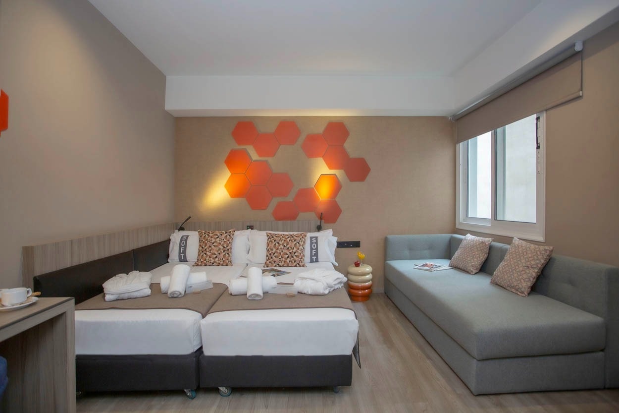 Modernes Hotelzimmer im Casual Kubic Athens, mit zwei Einzelbetten, Sofa und stilvoller Wanddekoration.