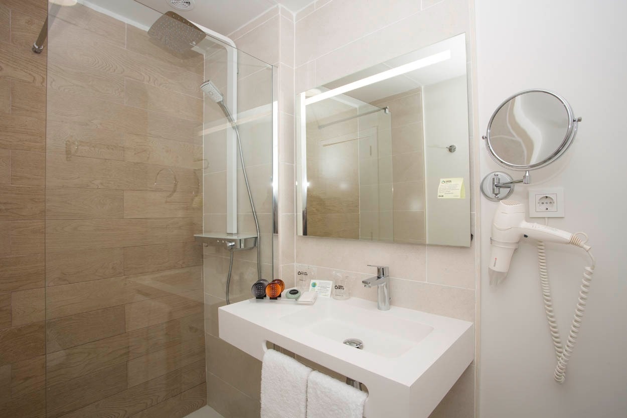 Modernes Badezimmer im Casual Inca Porto Hotel mit Dusche, Waschbecken und Haartrockner.