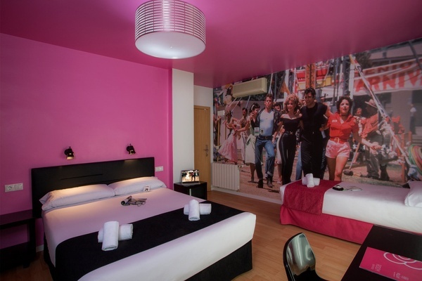 una habitación rosa con dos camas y un cartel de grease en la pared