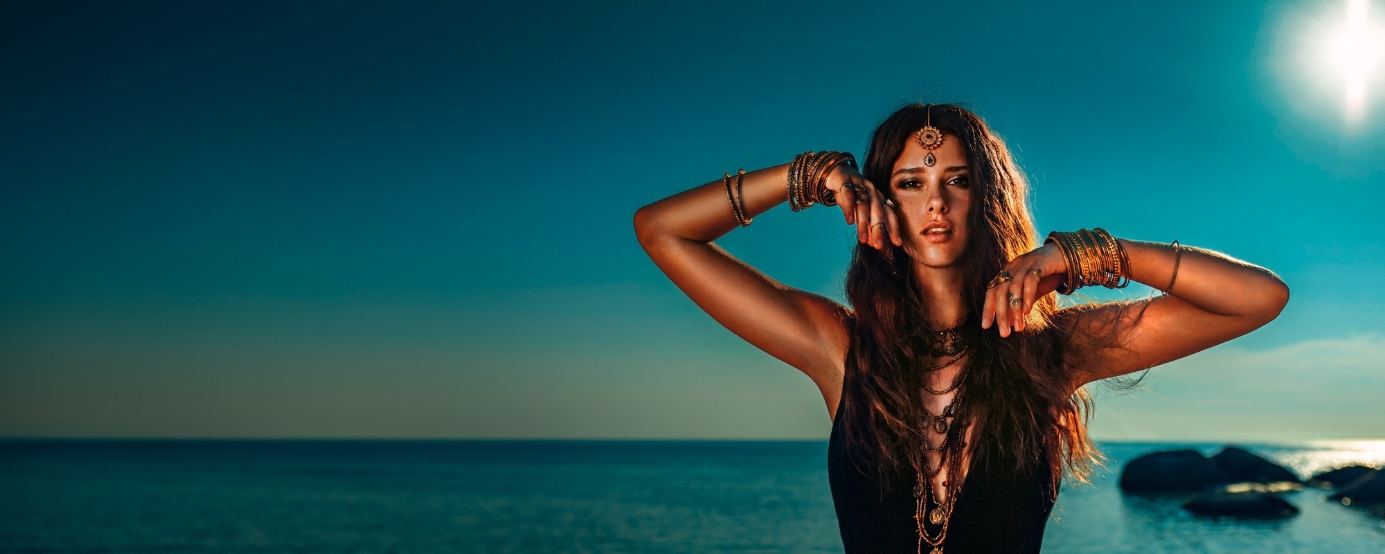 een vrouw met haar handen achter haar hoofd staat voor de oceaan