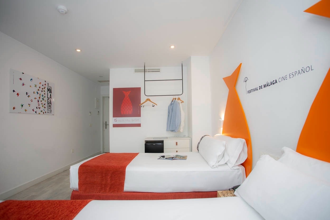 Zwei Einzelbetten mit orangen Decken in einem Zimmer des Casual del Mar Málaga, zentral gelegen.