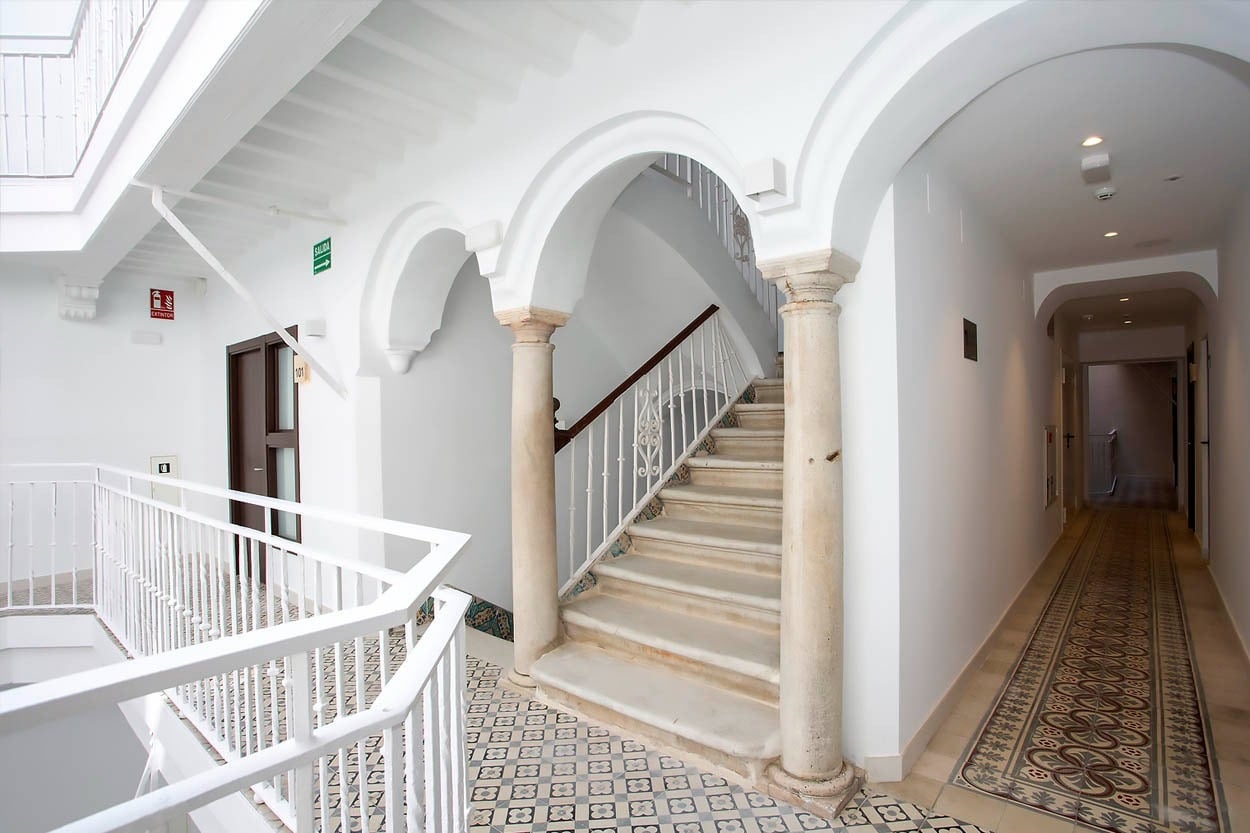 Elegante Innenansicht des Casual con Duende Cádiz - Hotel mit weißem Treppenhaus und historischen Böden.