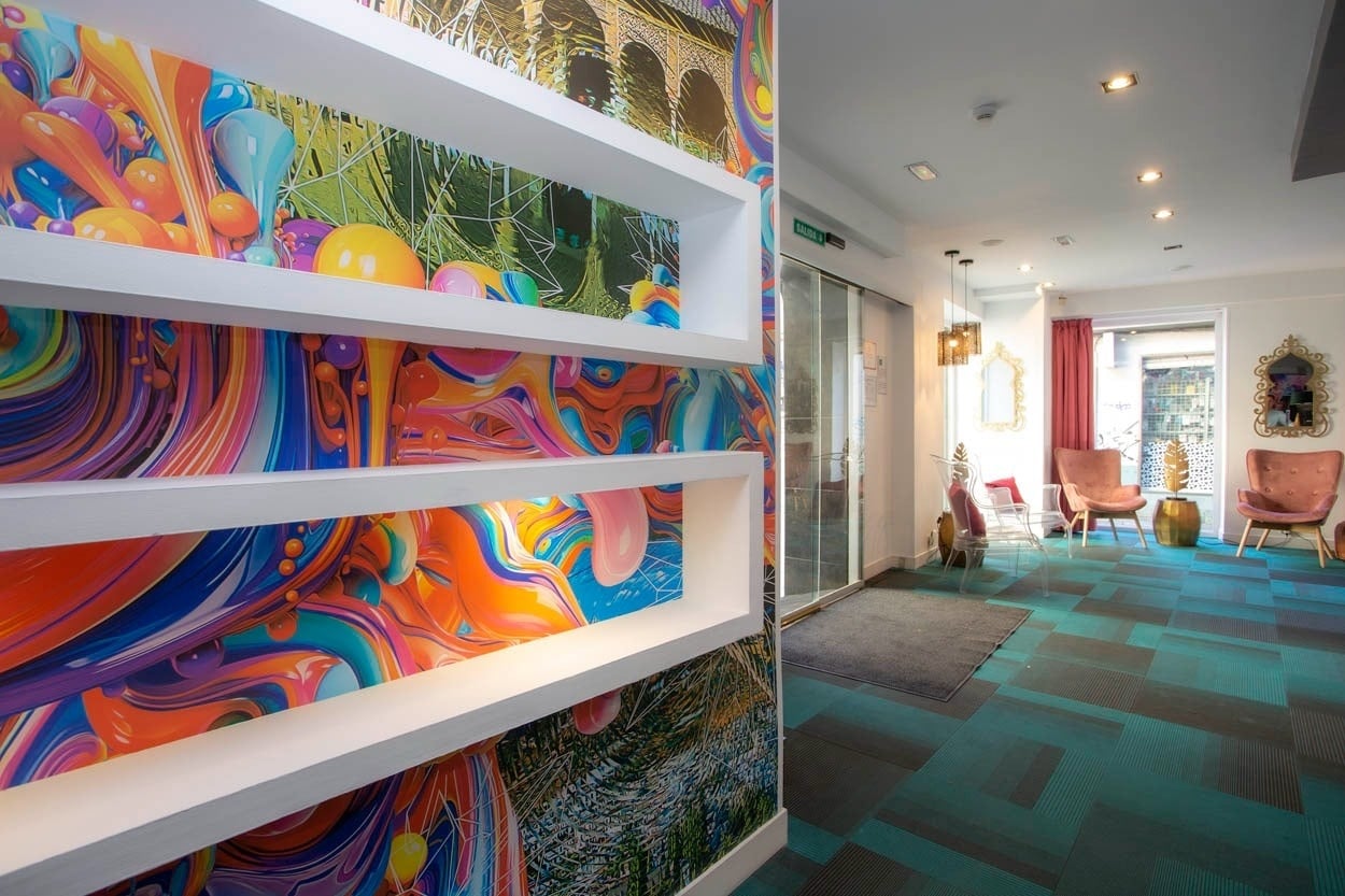 Pasillo del hotel Casual Ilbira Granada con papel tapiz vibrante y asientos coloridos.