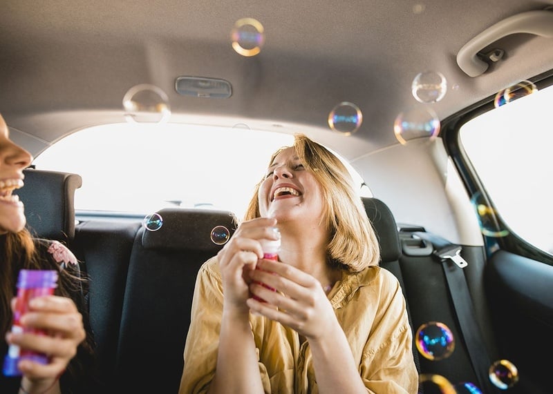 two women blowing soap bubbles in the back seat of a car