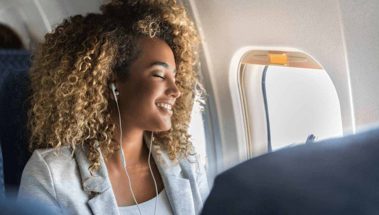Mujer sonríe en avión con auriculares, disfrutando un viaje casual corporativo.