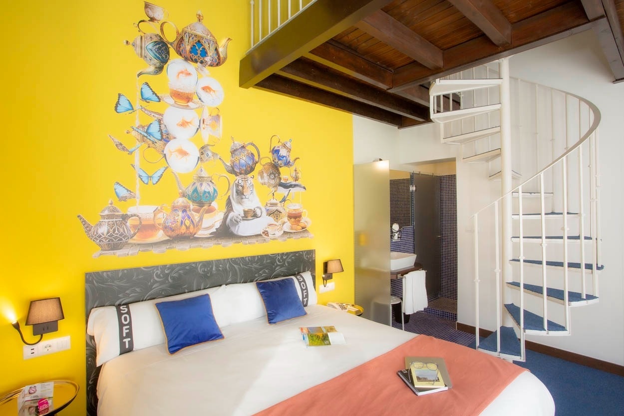 Habitación con mural de teteras y mariposas, cama cómoda y escalera de caracol. Casual Ilbira Granada.