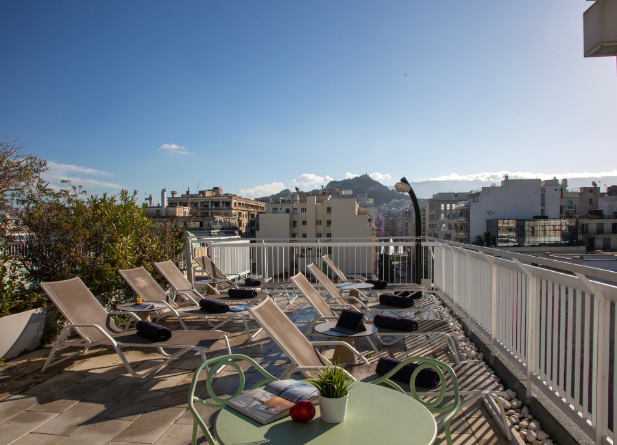 Relaxing hotel rooftop terrace with sunbeds, offering stunning city views and Lycabettus Hill.
