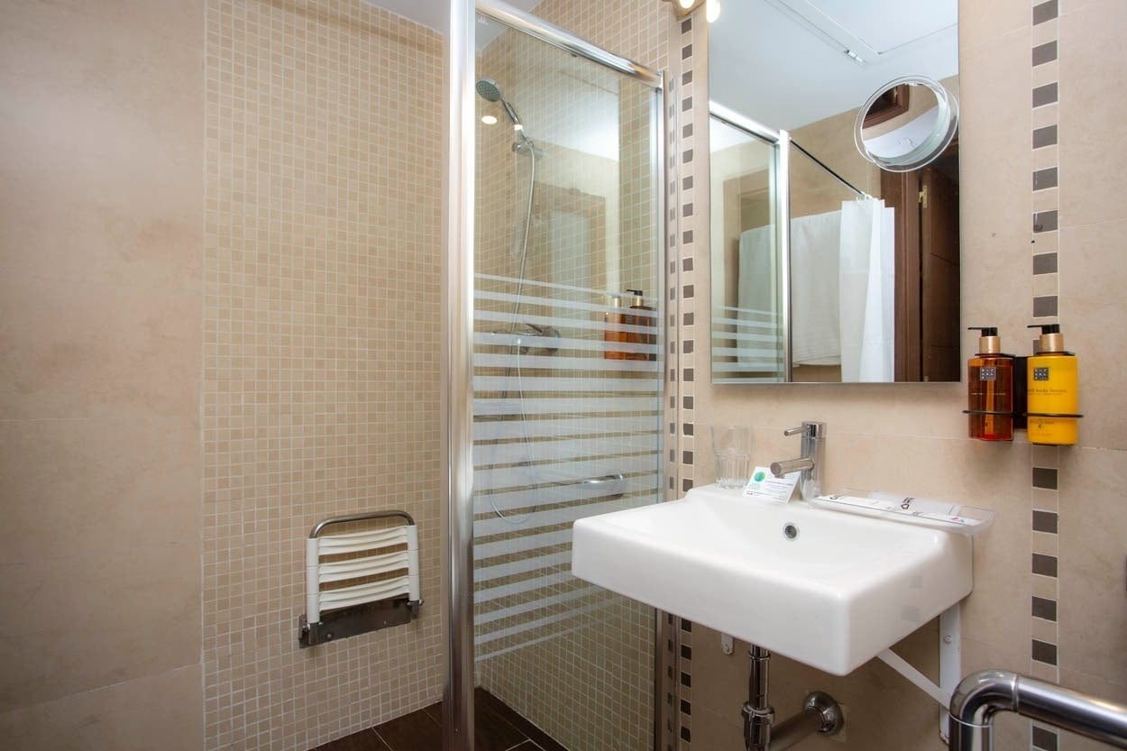 Baño moderno en Casual Ilbira Granada: ducha, lavabo y dispensadores de jabón.