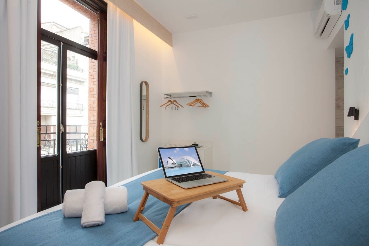 Habitación con cama, portátil en bandeja y balcón en Casual Socarrat Valencia.