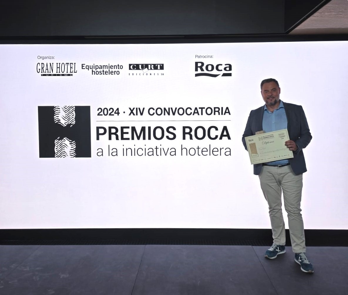 un hombre sostiene un certificado frente a un cartel que dice premios roca