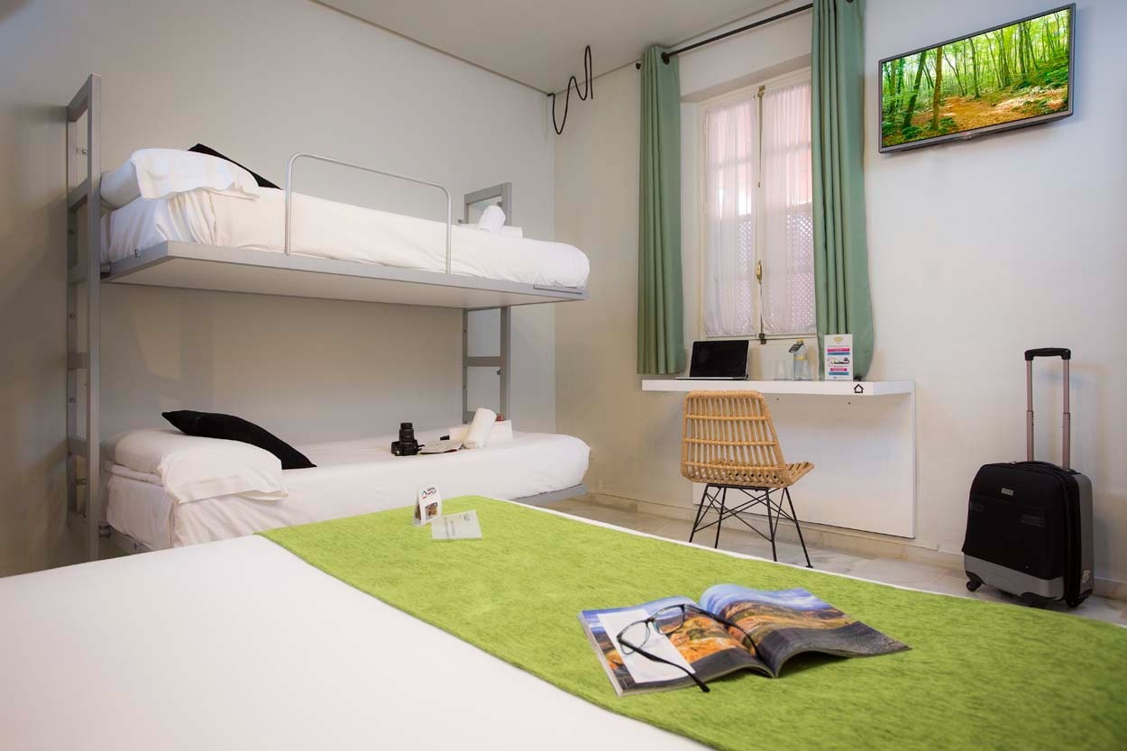 Doppelbett im Casual de las Letras Sevilla Hotel mit grüner Tagesdecke, Schreibtisch und Fernseher