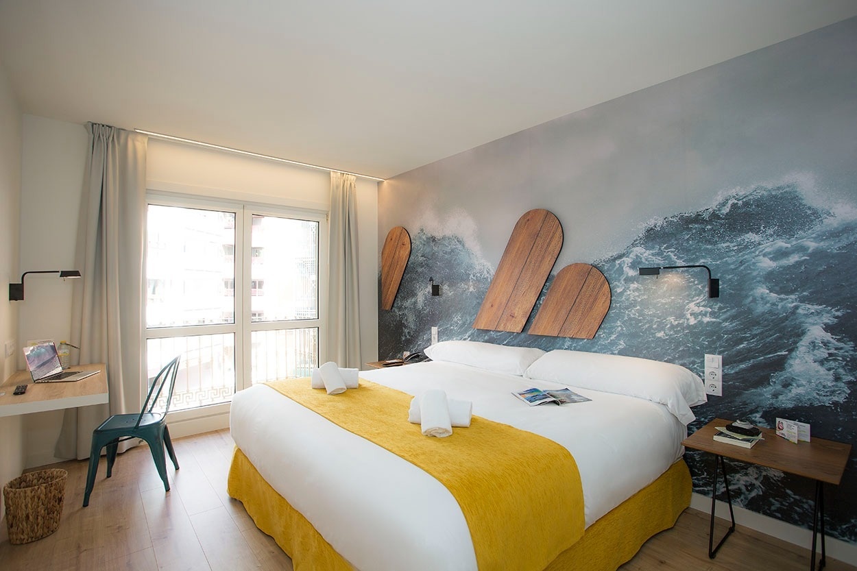 Modernes Hotelzimmer mit Wellen-Thema, Doppelbett, Schreibtisch und Fenster. Casual de las Olas San Sebastián.