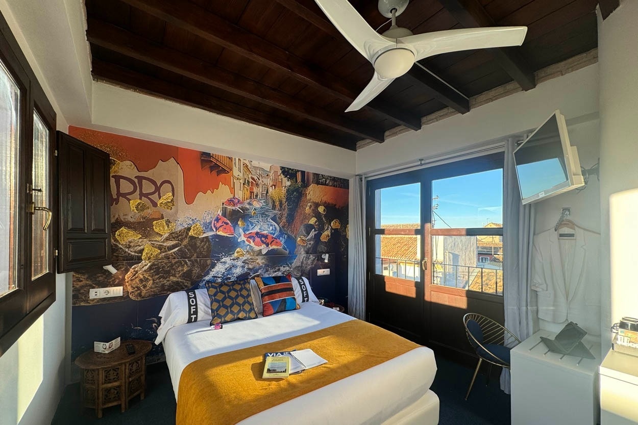 Habitación Casual Ilbira Granada: cama confortable, mural artístico y balcón con vistas.