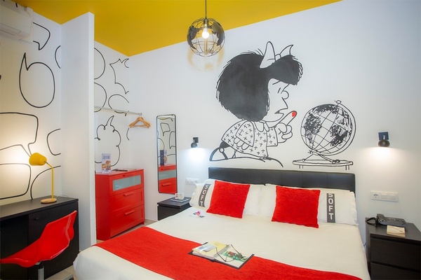 une chambre avec un lit et des oreillers avec un dessin de mafalda sur le mur