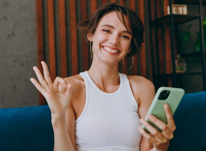 une femme fait un signe ok tout en tenant un téléphone portable