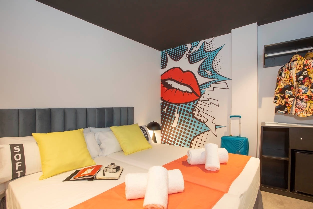 Casual Pop Art Benidorm: Doppelbett mit Pop-Art-Wandbild und gelben Kissen. Hotel im Pop-Art-Stil in Benidorm.