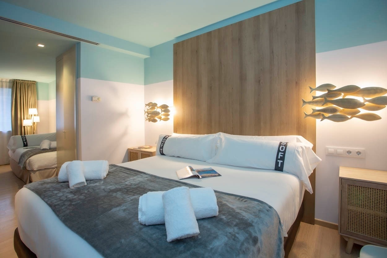 Een sfeervol hotelbed met witte lakens en een grijze deken, verlicht door visvormige lampen, in Casual Colours Barcelona.