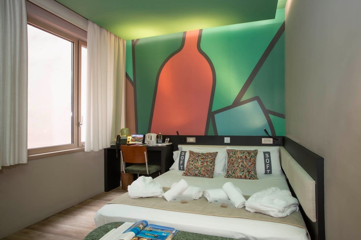 Modernes Hotelzimmer: Bett mit Kissen, Schreibtisch und großer Fensterfront im Casual Kubic Athens - Smart Hotel im Zentrum von Athen.